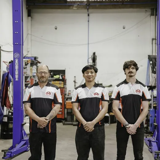 Three Waiwakaiho Auto Services technicians beside a vehicle hoist